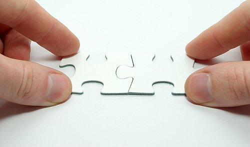 Hände legen ein zweiteiliges Puzzle